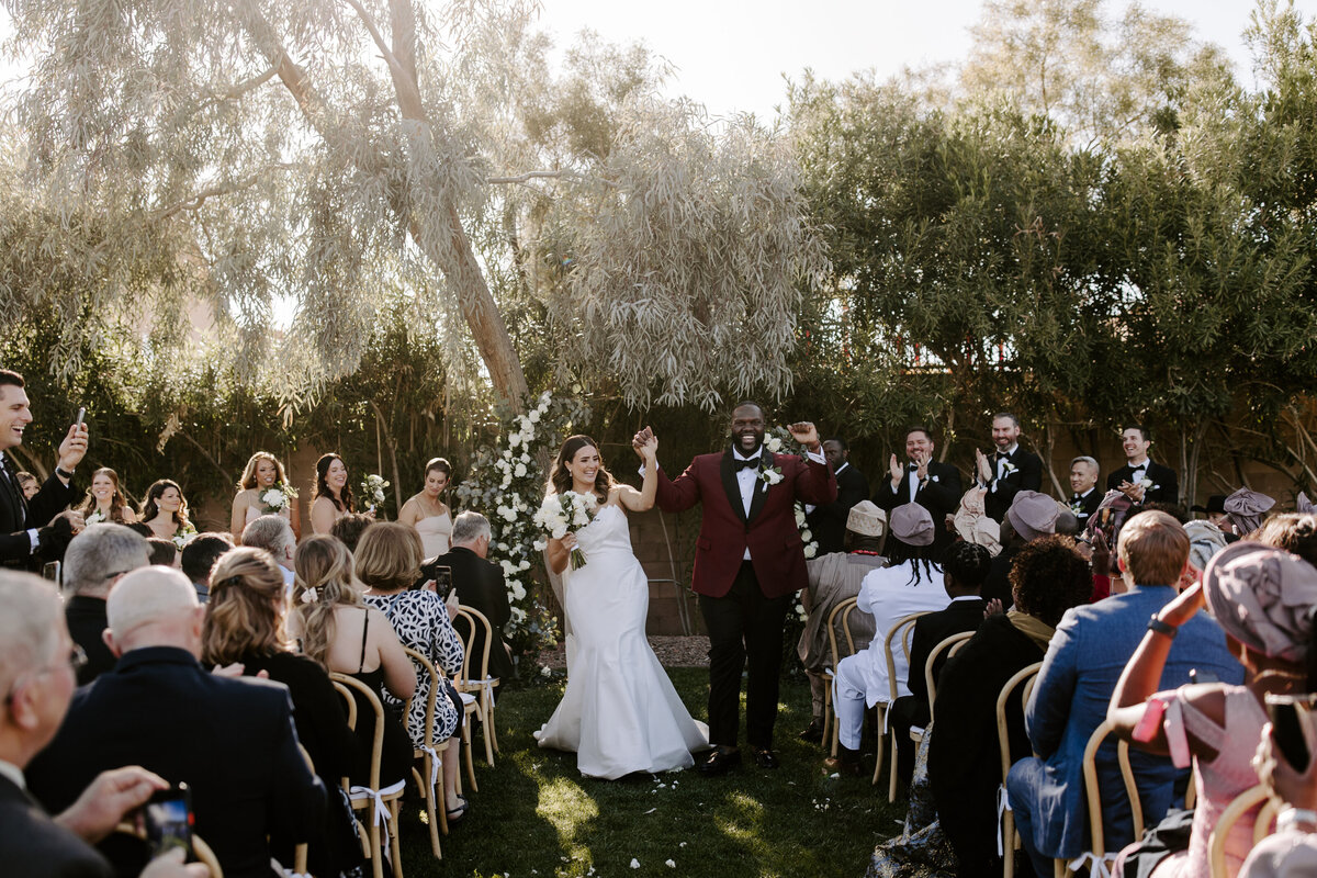 A couple holds hands as they walk back down the aisle after getting married at The Lotus House.