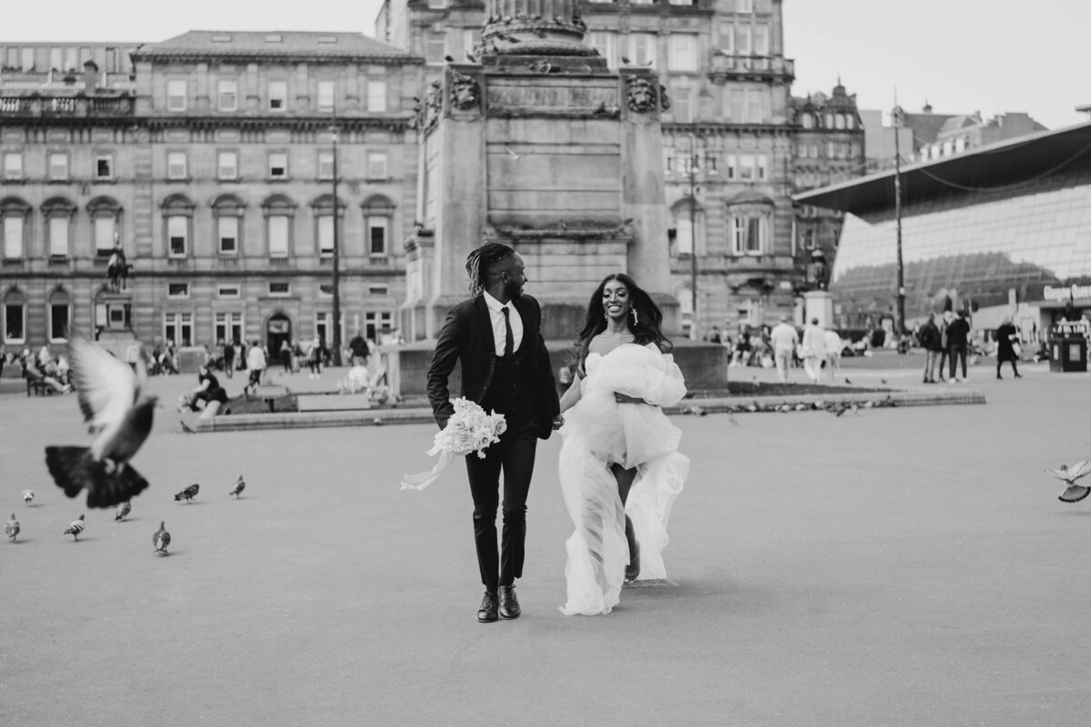 A bride and groom run through a city centre square in Glasgow following their Scottish elopment.