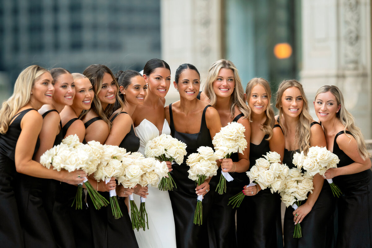 Bride in white wedding dress surrounded by Bridesmaids in black dresses holding white flowers