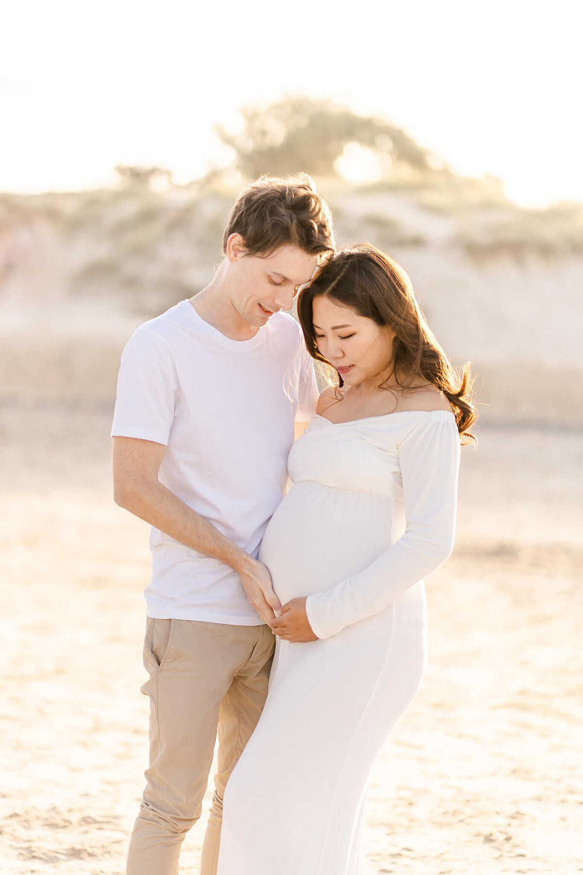 Backlit pregnancy portrait couple touching belly bump on The Spit Gold Coast