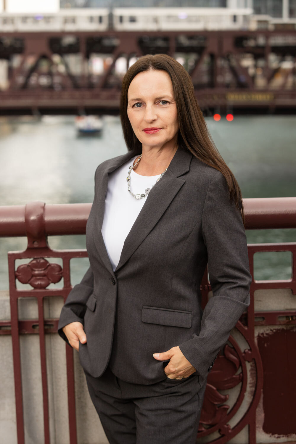 Woman in gray suit standing confidently in front of a river bridge