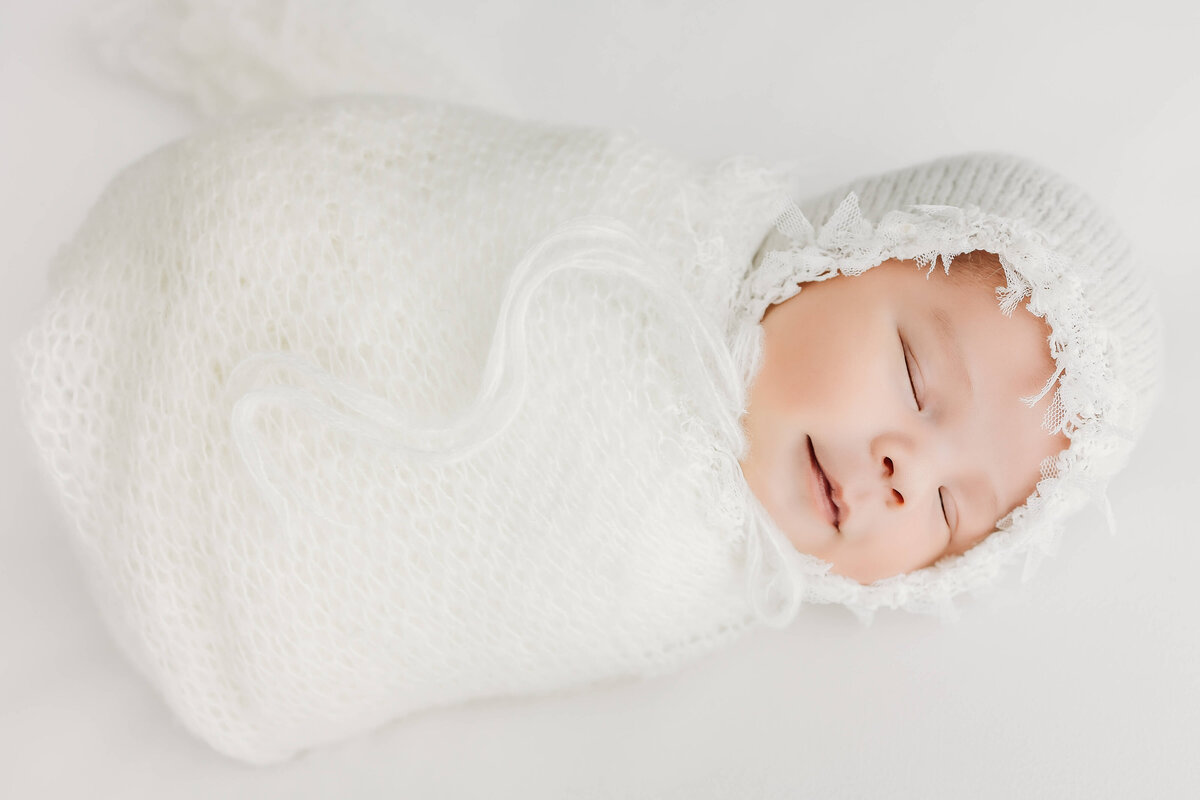 Wrapped smiling baby in bonnet all white background