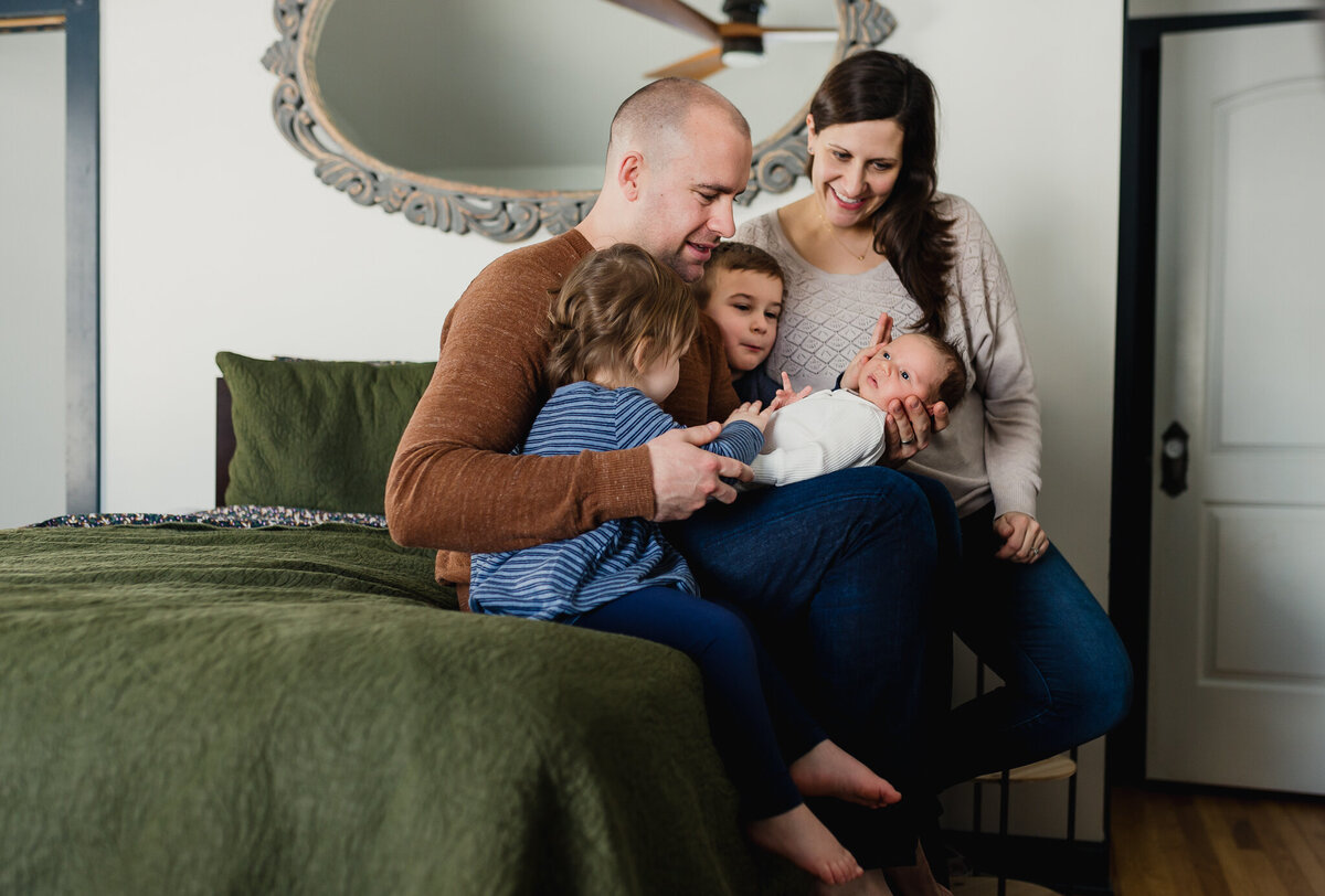 Family photographer capturing a whole family snuggles newborn on bed