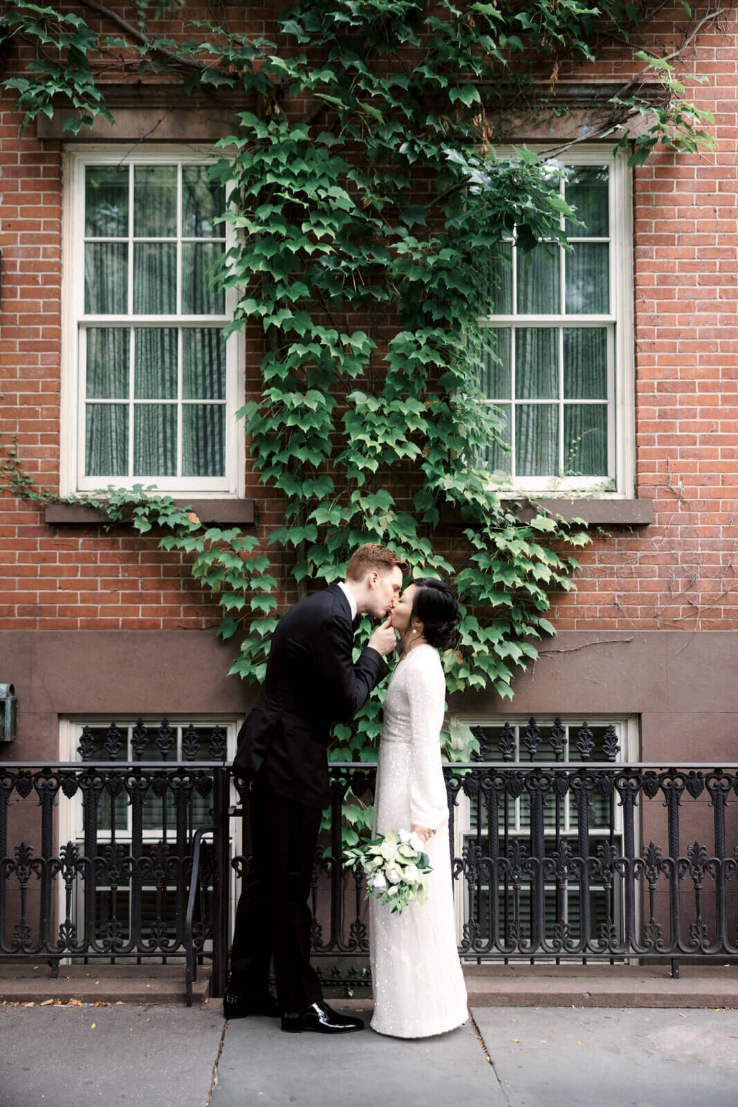 The bride and the groom are kissing on a sidewalk along the streets of West Village, NYC. Image by Jenny Fu Studio