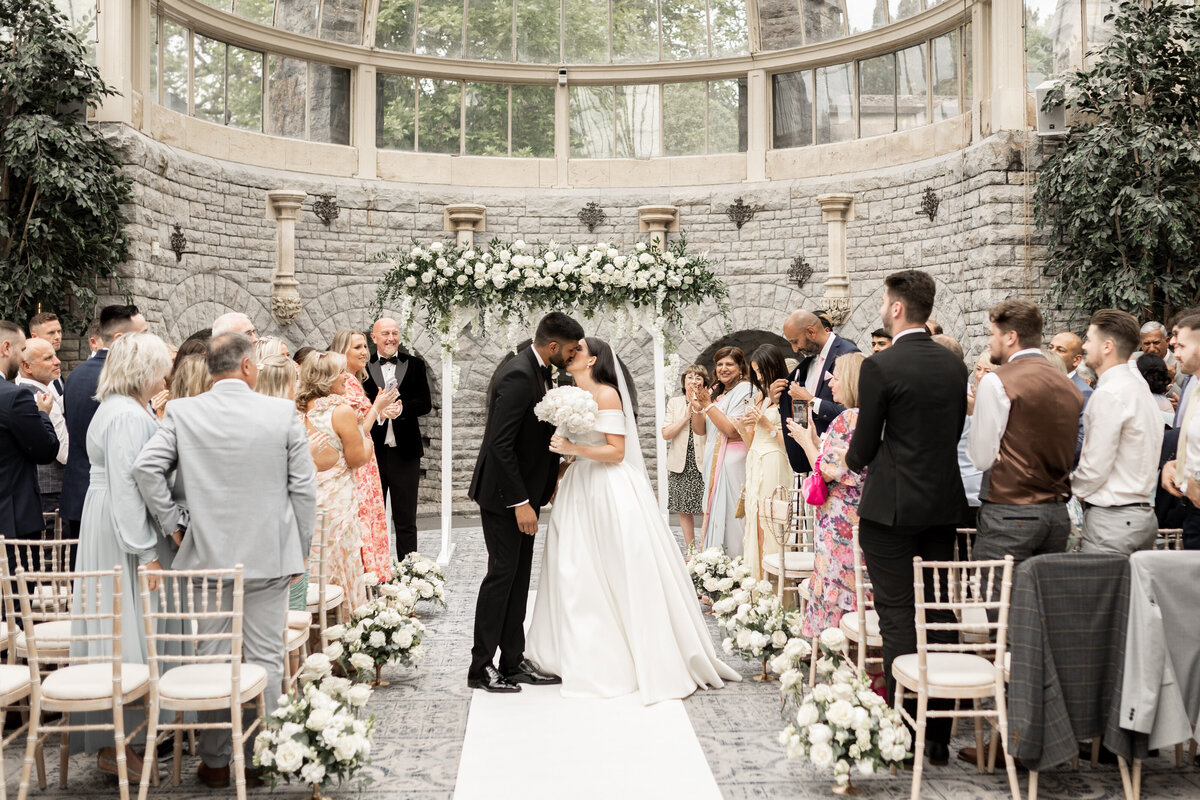 The bride and groom share their first kiss during their wedding ceremony at Wedding ceremony in the Orangery at Tortworth Court, Cotswold wedding venue