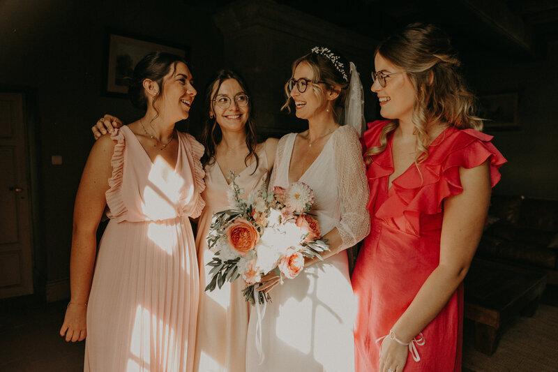 Mariée entourée de trois de ses demoiselles d'honneur habillées de robes couleurs pastels et corail lors d'une séance photo mariage en vendée.