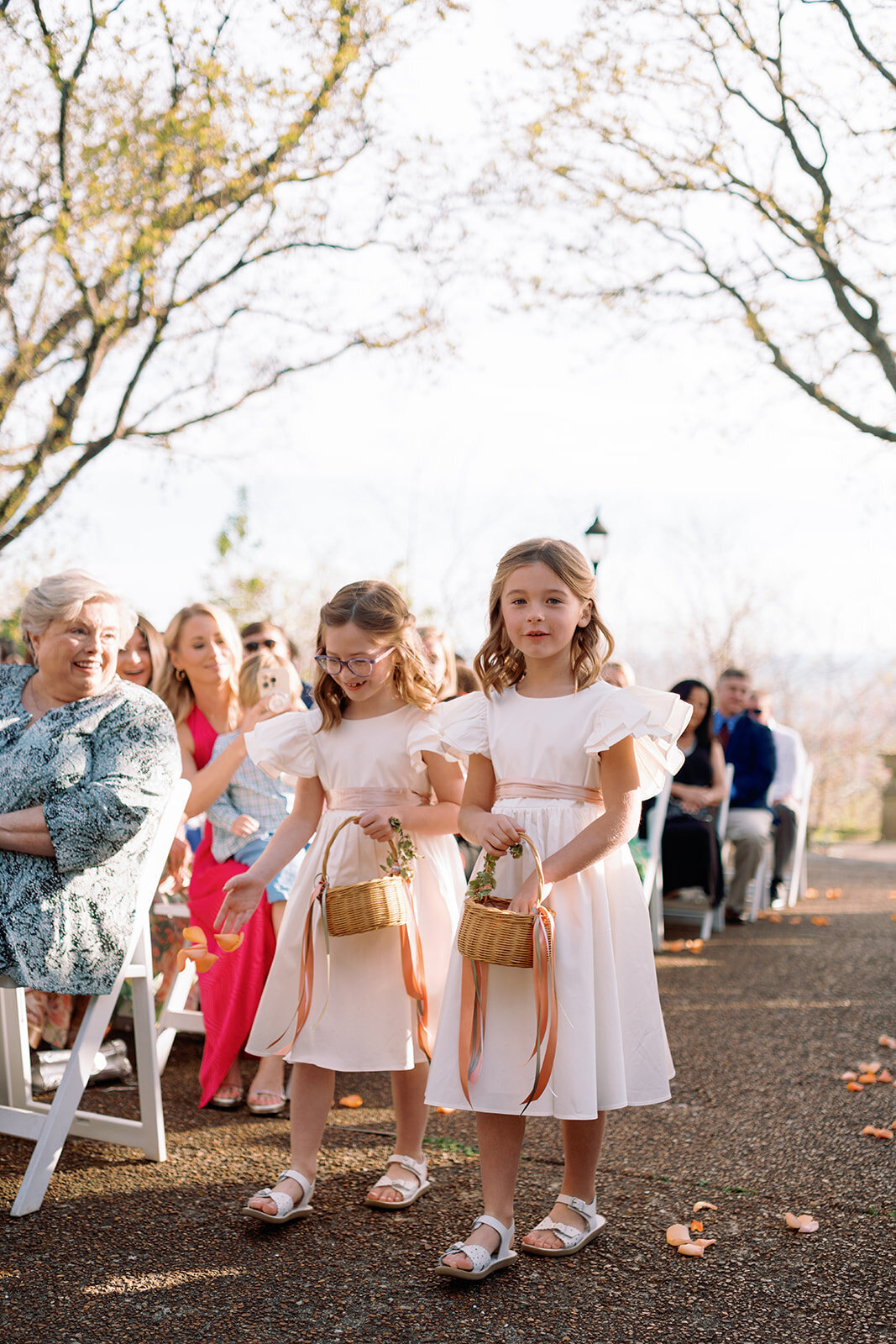 Two young flower girls in white dresses walk down the aisle holding small baskets during the wedding ceremony at Burritt on the Mountain in Huntsville, Alabama, photographed by Perry Hancock.