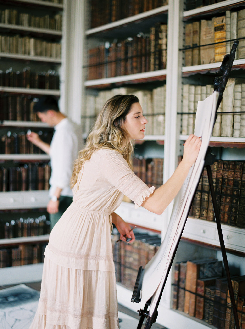 Woman drawing and man looking for a book in old library in Los Angeles