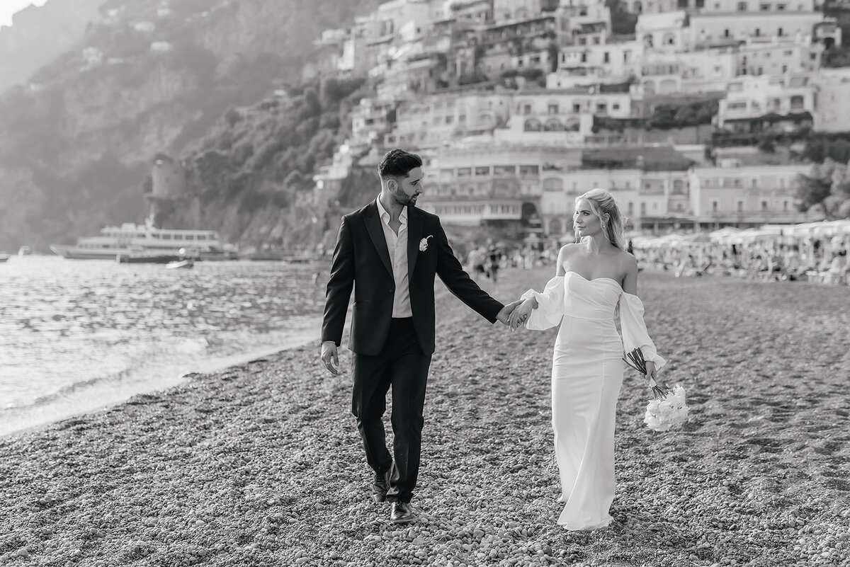 Bride and Groom walking hand in hand along the stone beach in Positano