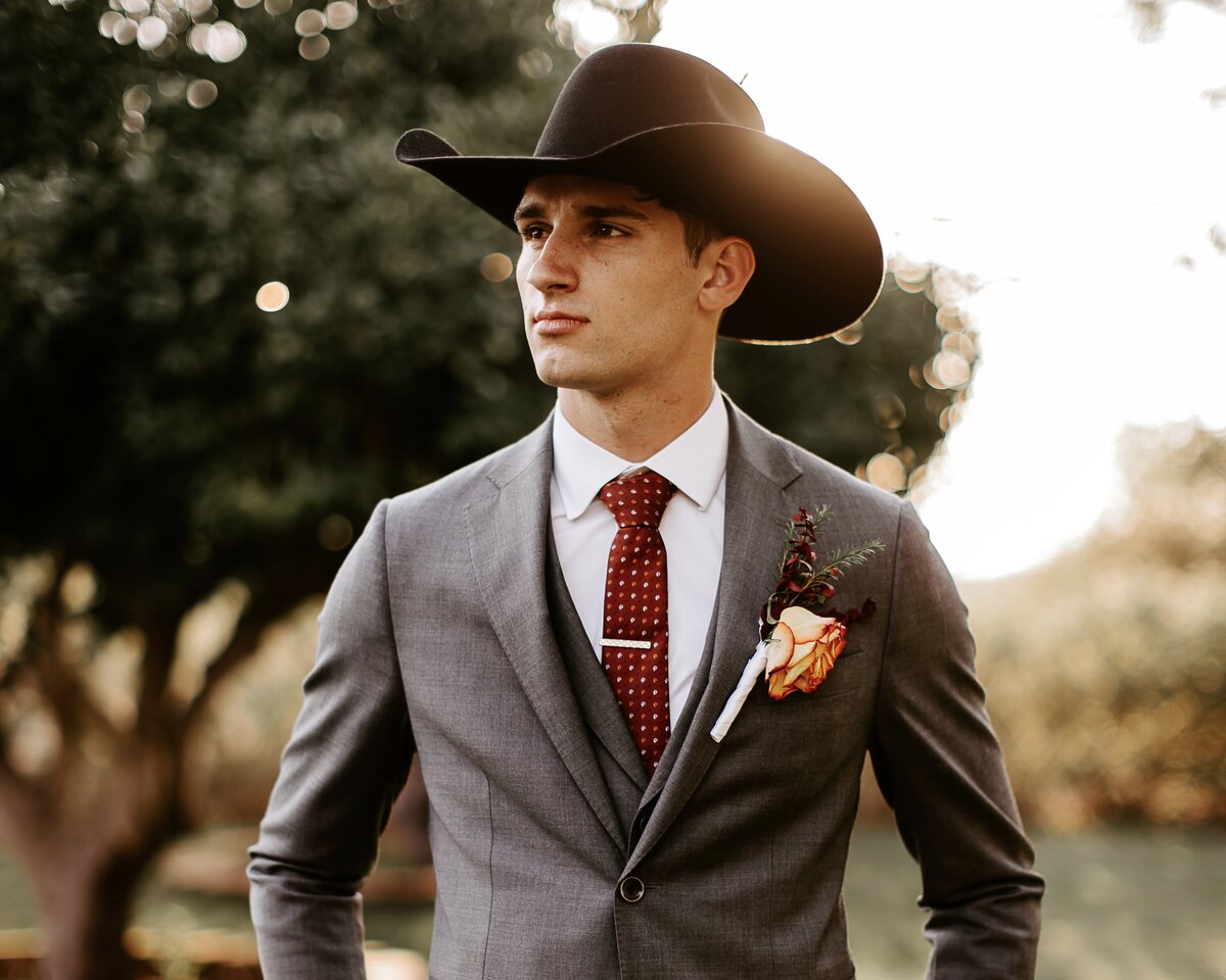 A western groom wearing a cowboy hat and cowboy boots with a grey suit