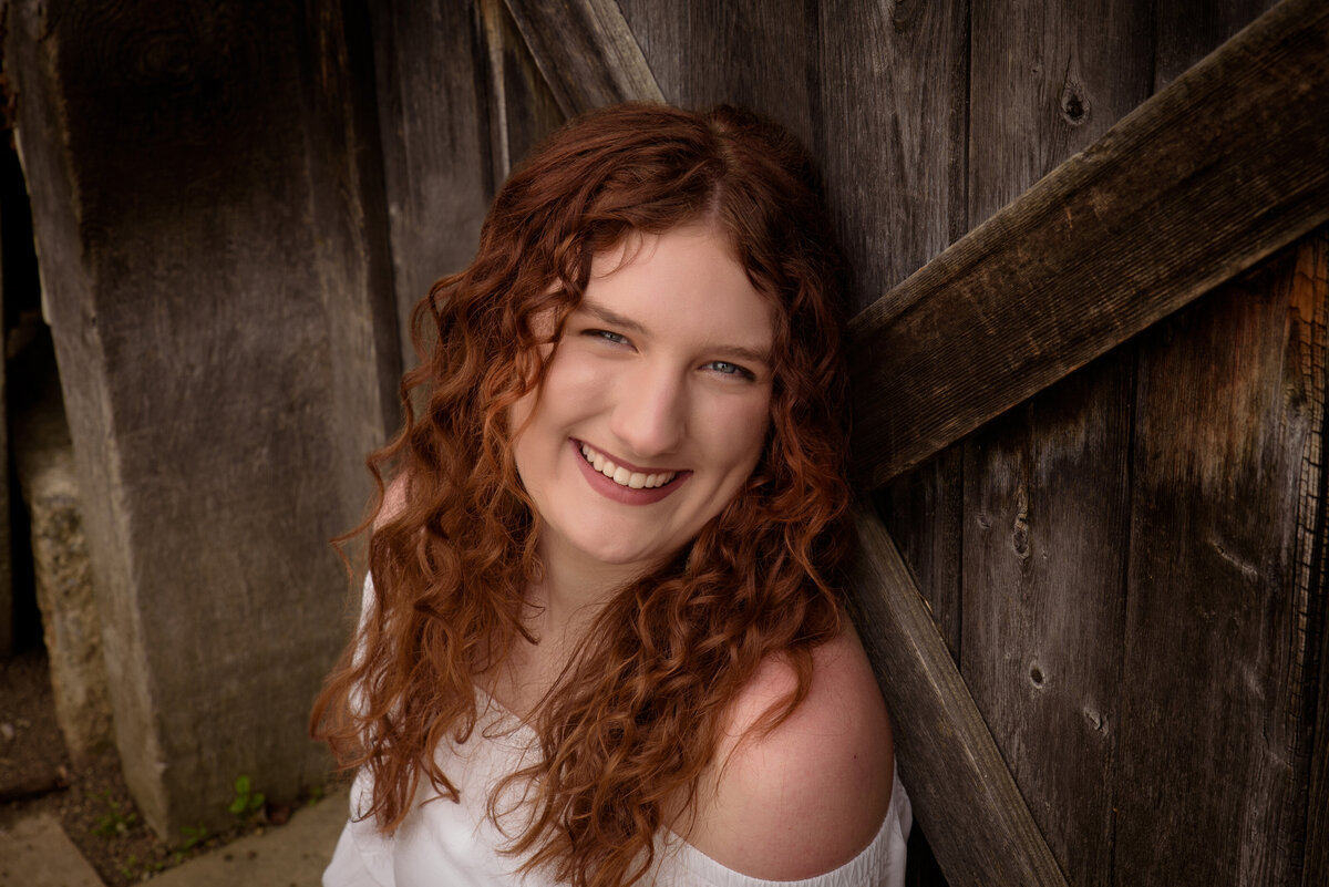 Green Bay East High School senior girl wearing a white sleeveless shirt and bell bottom leaning against wooden door in the flower gardens at the Green Bay Botanical Gardens in Green Bay, Wisconsin.