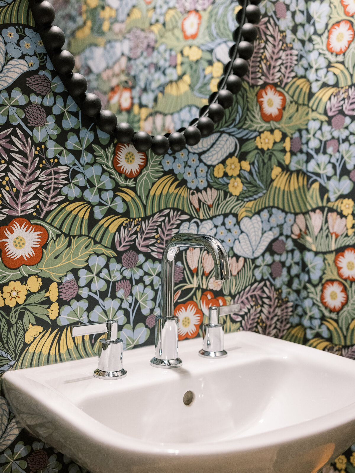 Black floral powder room with a black beaded mirror