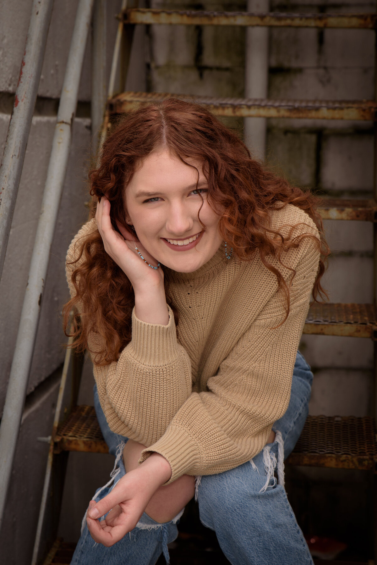 Green Bay East High School senior girl wearing a tan sweater and jeans sitting on metal stairs in an urban setting in downtown Green Bay, Wisconsin