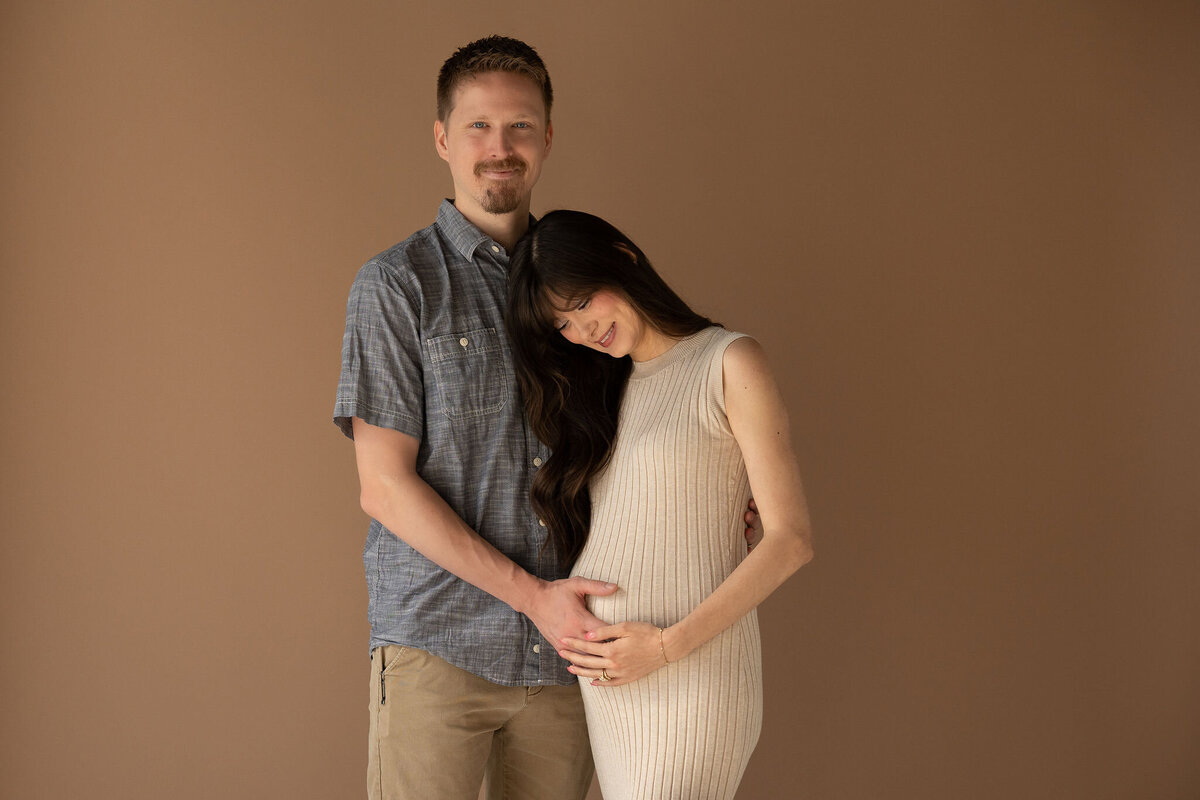 A couple standing close together each with one hand on a pregnant stomach 