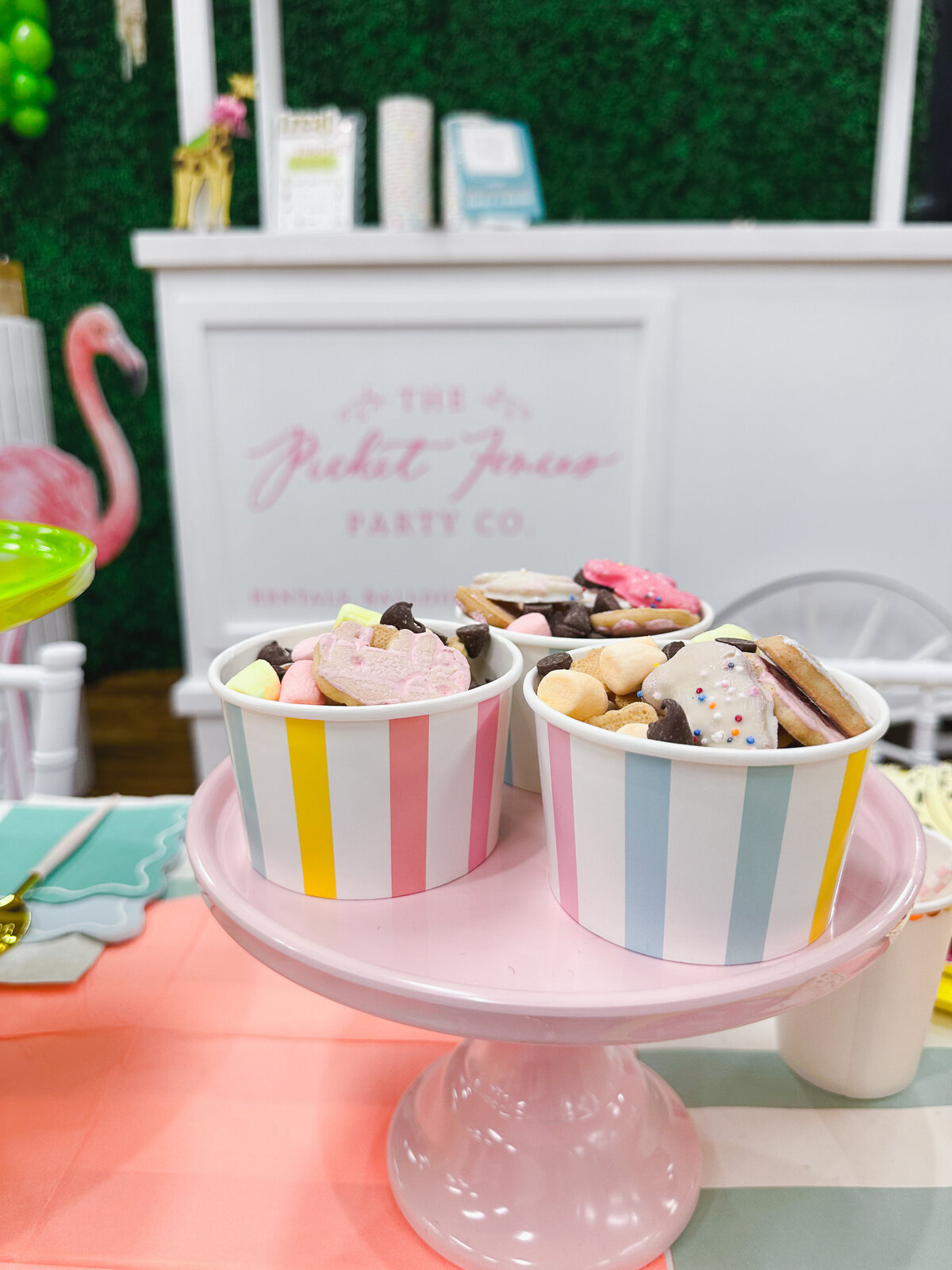 Striped treat cups on a pink cake stand holding animal cracker snack mix. 