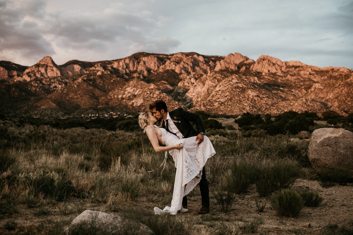 groom dipping wife in front of desert mountain