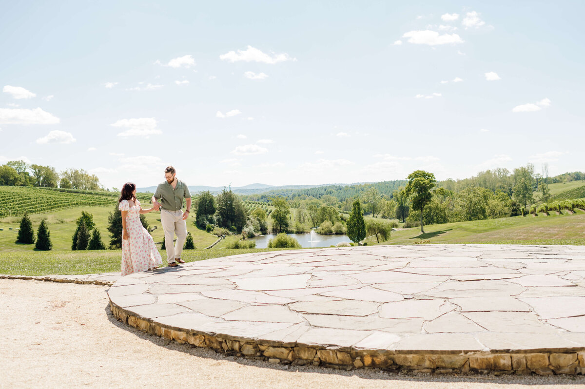 stone tower winery wedding venue with woman and man holding hands and walking up to a stone platform with rolling hills through the distance until they hit the mountains