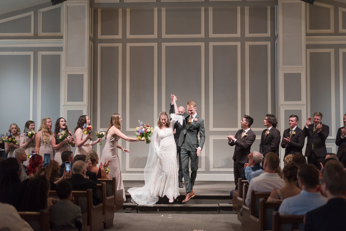 denver wedding photographer captures bride and groom holding their hands together in the air as they leave their wedding ceremony