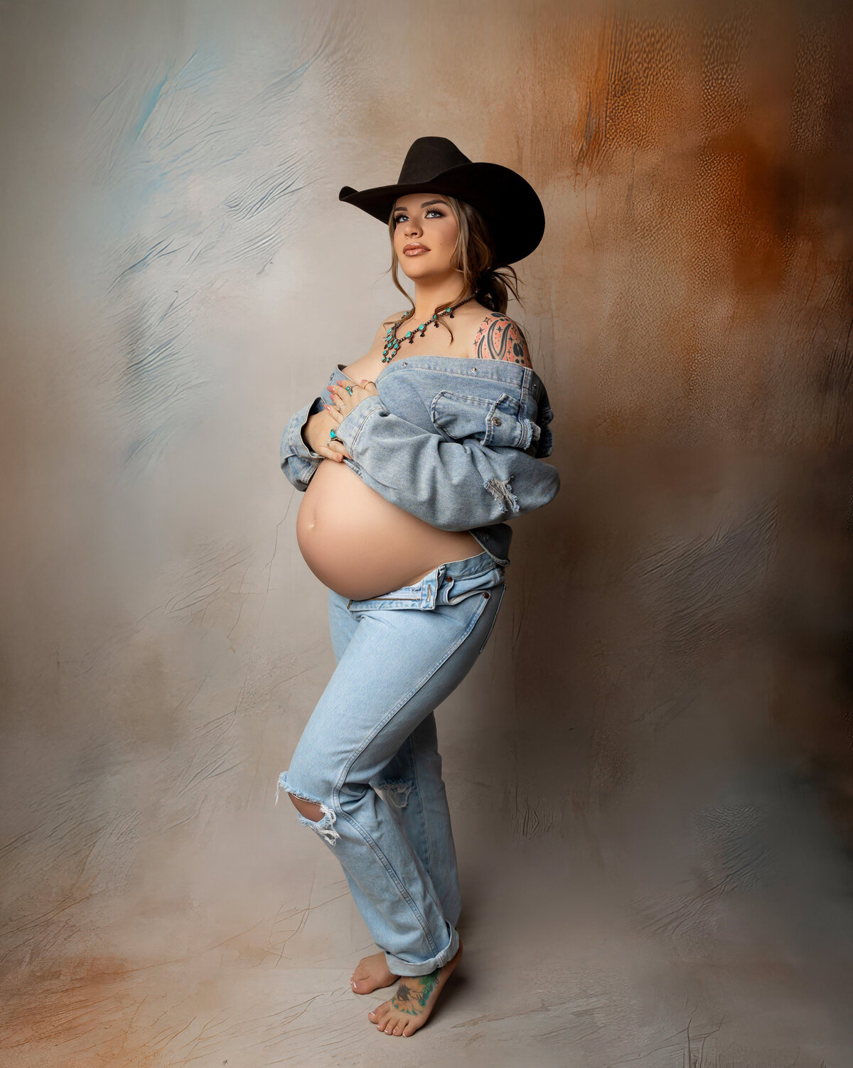 Elegant maternity portrait of a glowing expectant mother dressed in rustic cowboy attire, set against a warm, earthy-toned backdrop. Captured by Inland Empire maternity photographer Kaitlyn Dawn Photography.
