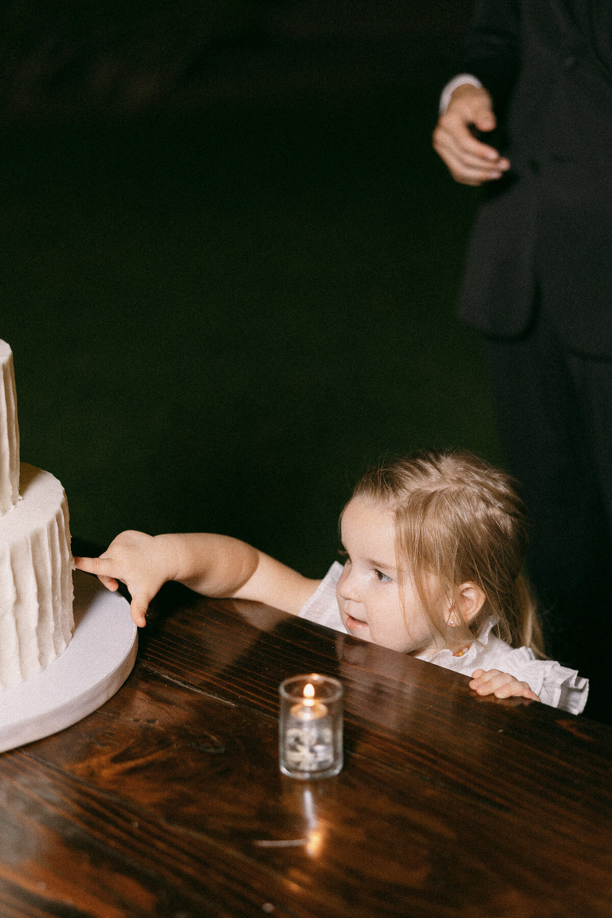 A child reaching her hand out to touch a wedding cake.