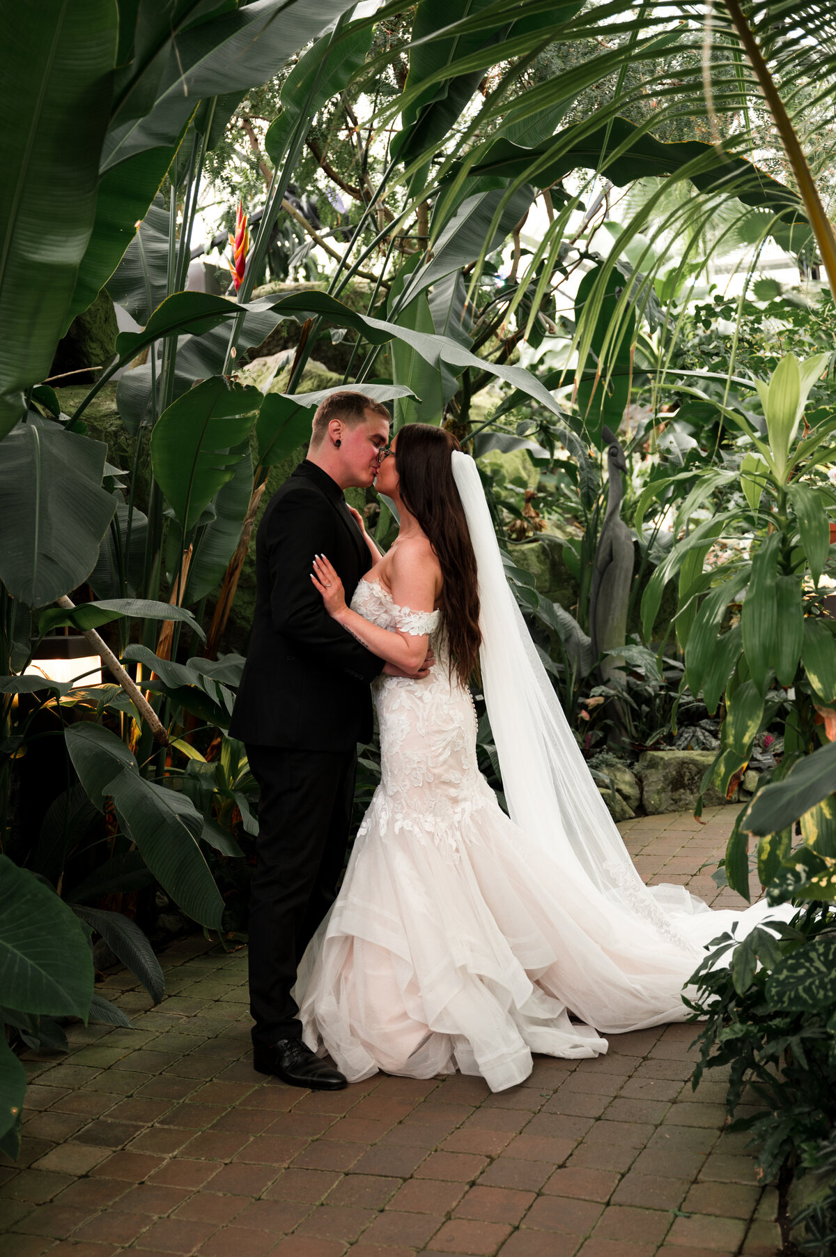 bride and groom on a pathway with tropical plants hanging over them