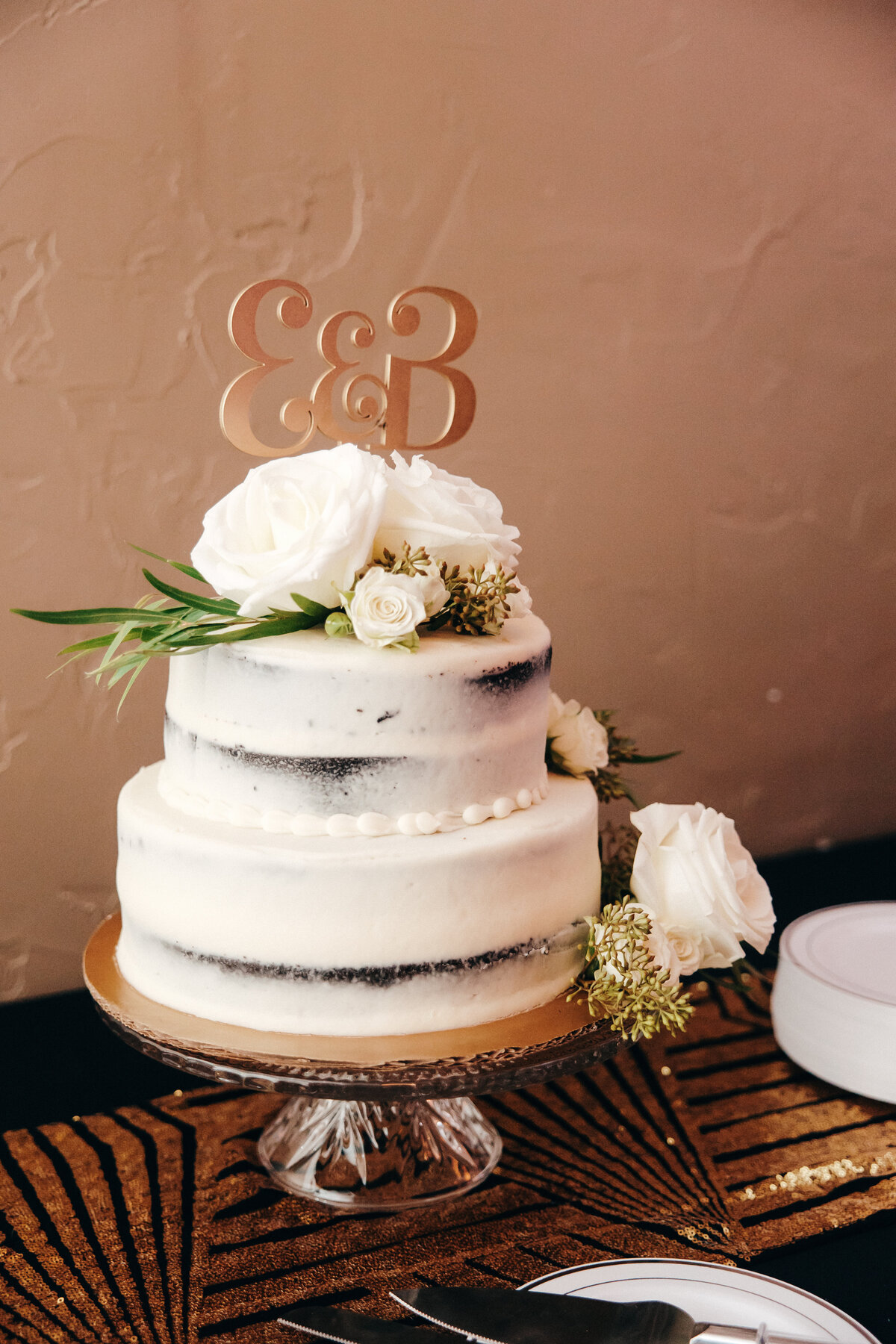 White wedding cake with white flowers and an initial cake topper.