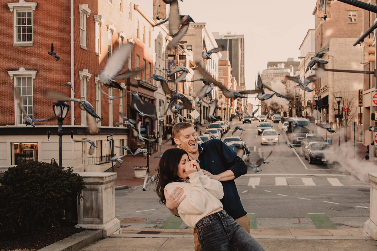 A couple laughing and leaning back as birds fly around them 