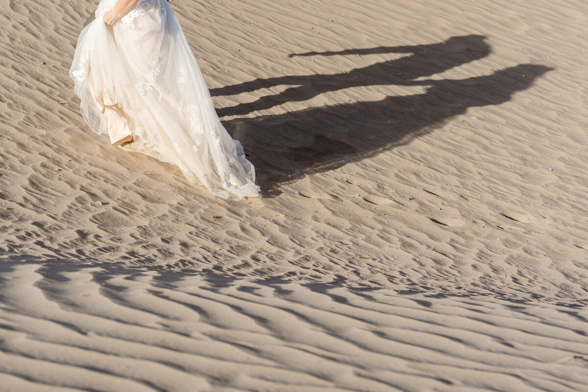 A person in a wedding dress walking up a sand dune