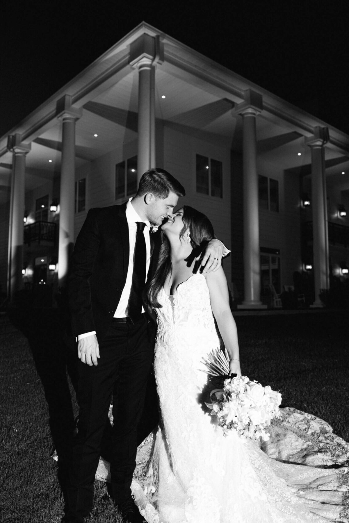 A black and white wedding photo of the bride and groom in front of their wedding venue legacy acres