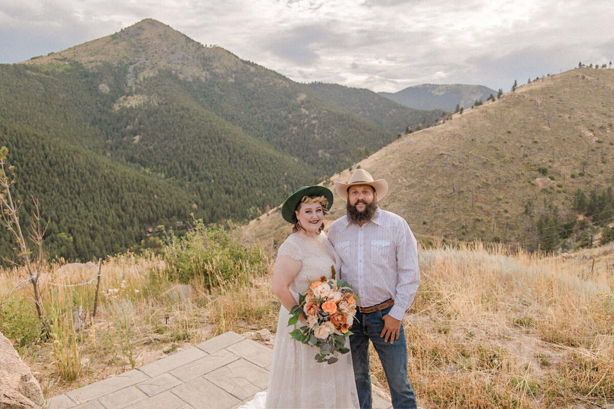 The bride and groom  embrace and smile for the camera in front of a stunning mountain overlook