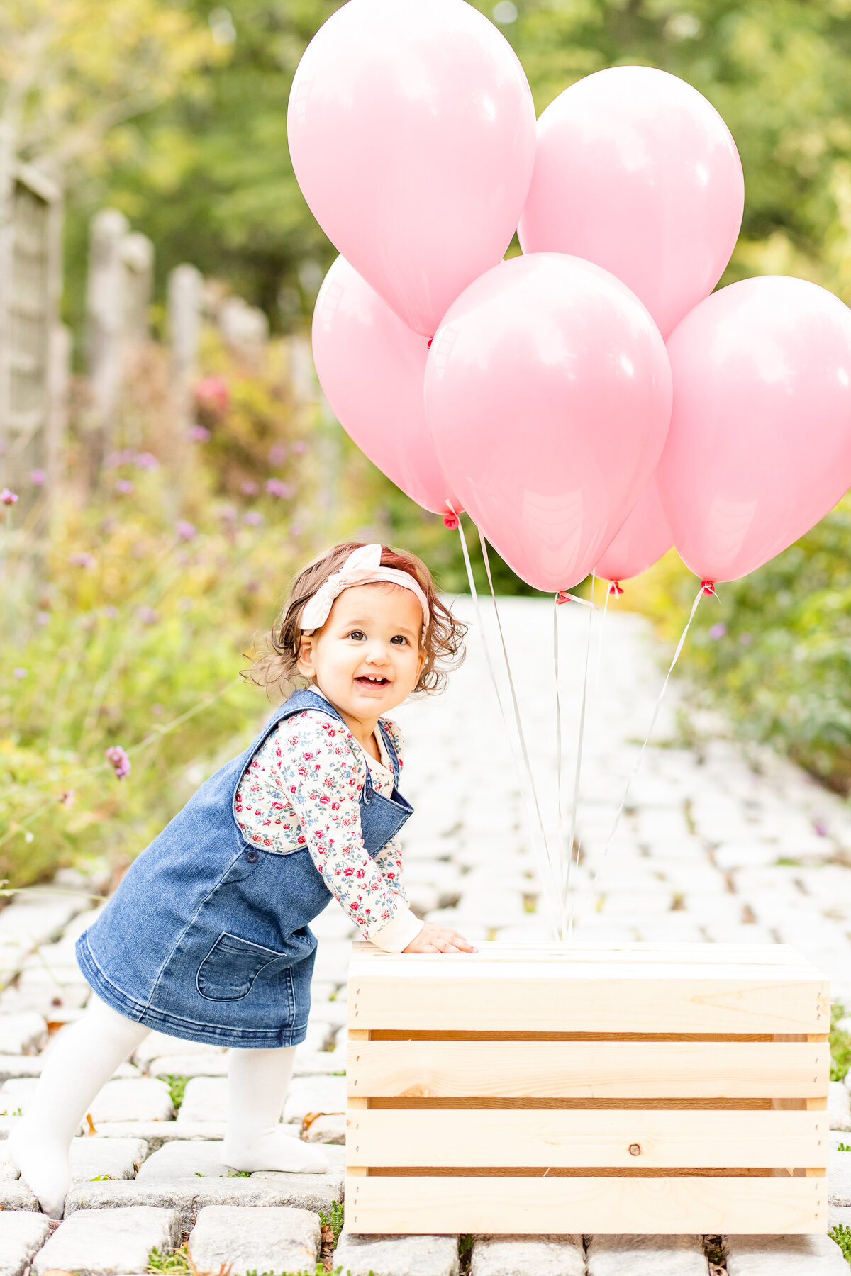 First birthday girl with pink balloons smiling at camera