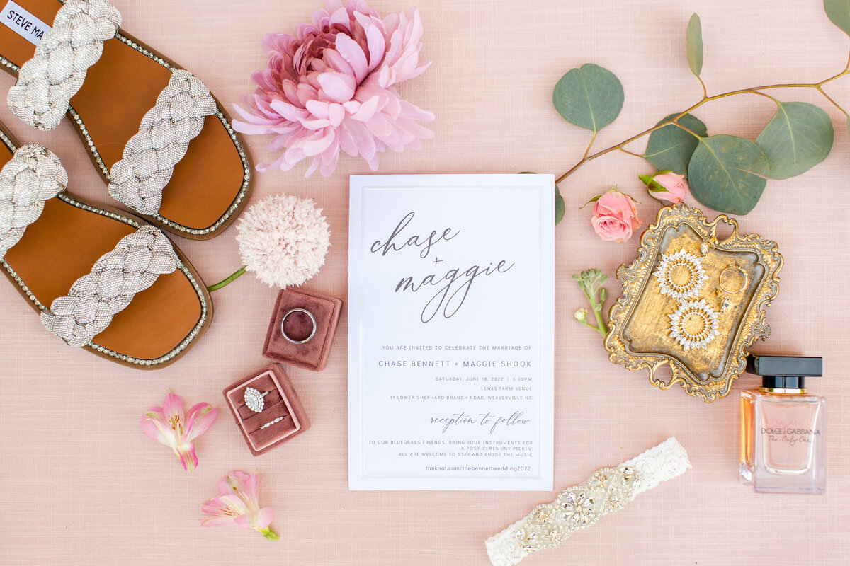 flat lay photo with wedding invitation and rings with pink tones