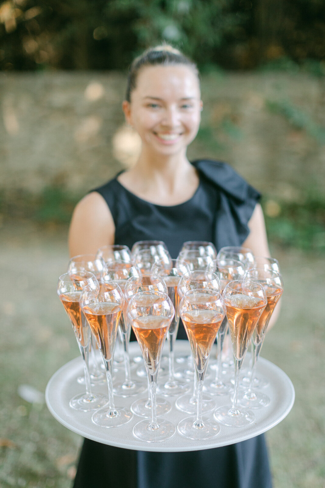 Waitress serving glasses of rosé champagne during luxury wedding cocktail in Provence.
