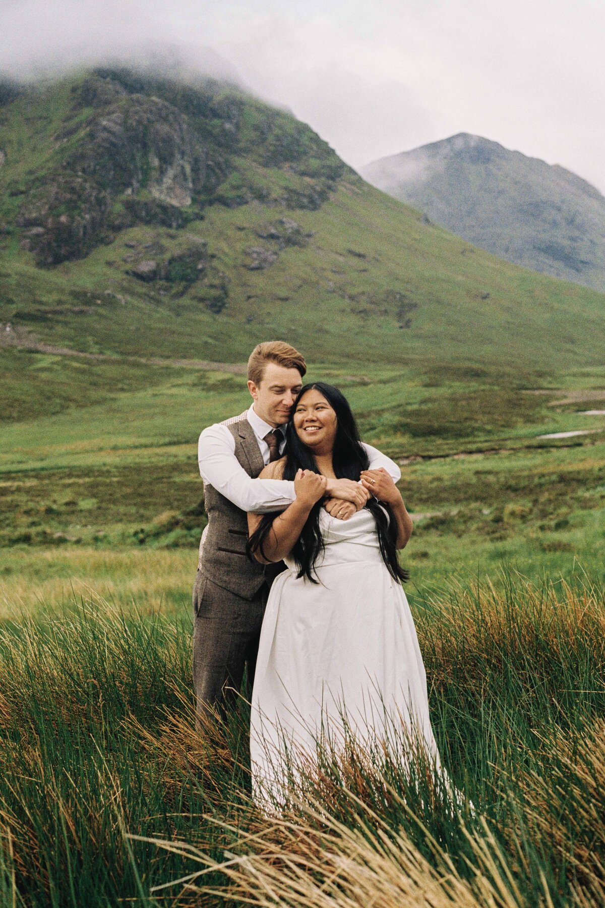 A couple wrap their arms around each other and Glencoe is seen behind them.