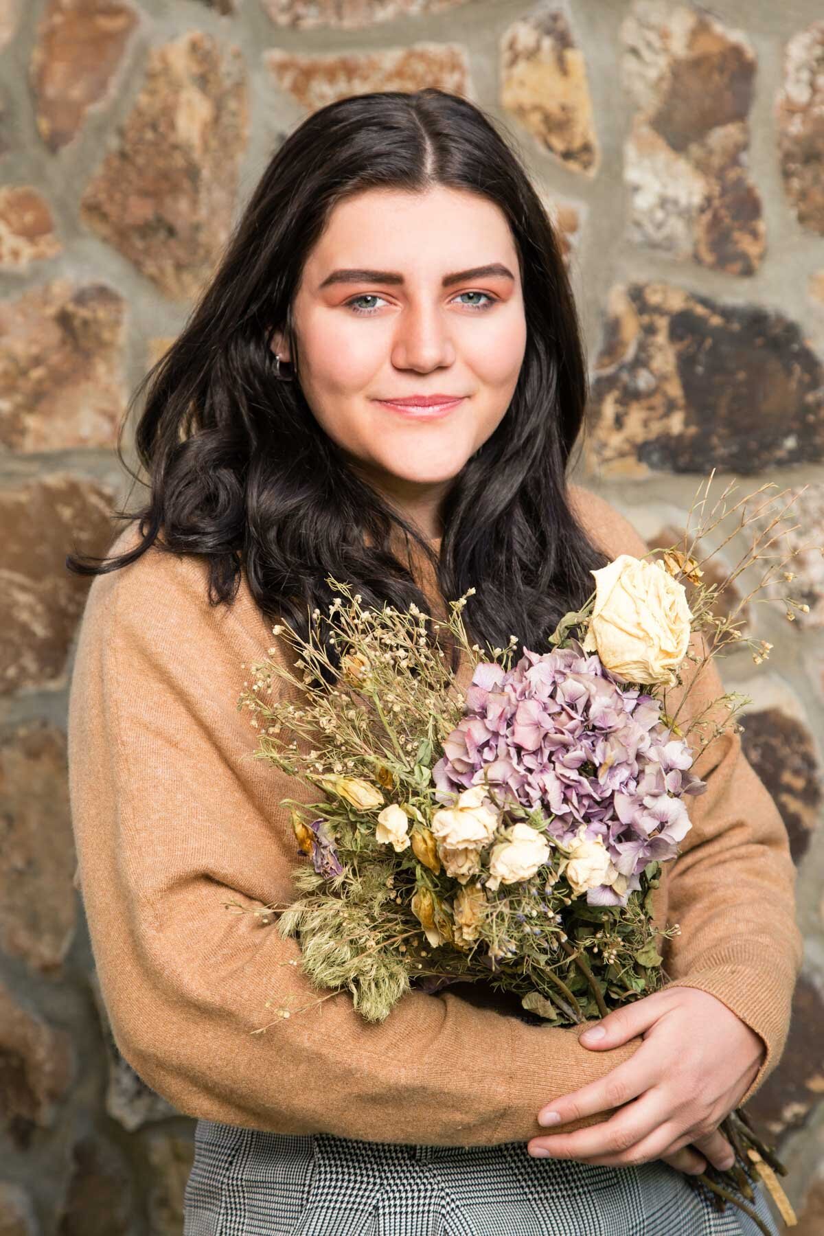 Senior girl posing against a rock wall with flower bouquet in Lehi, Utah.