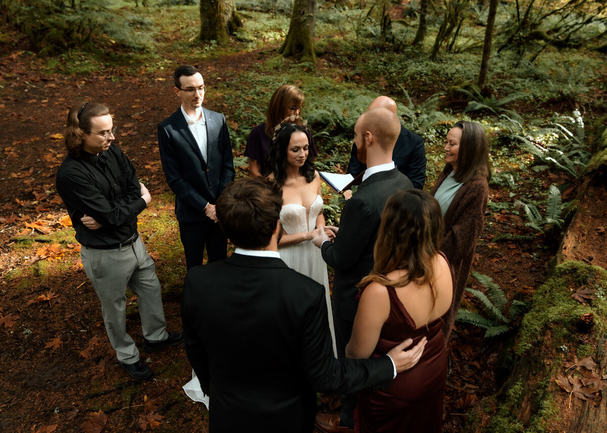 Aerial view of bride and groom being married by the groom's father, surrounded by their closest family and friends in the Oregon forest