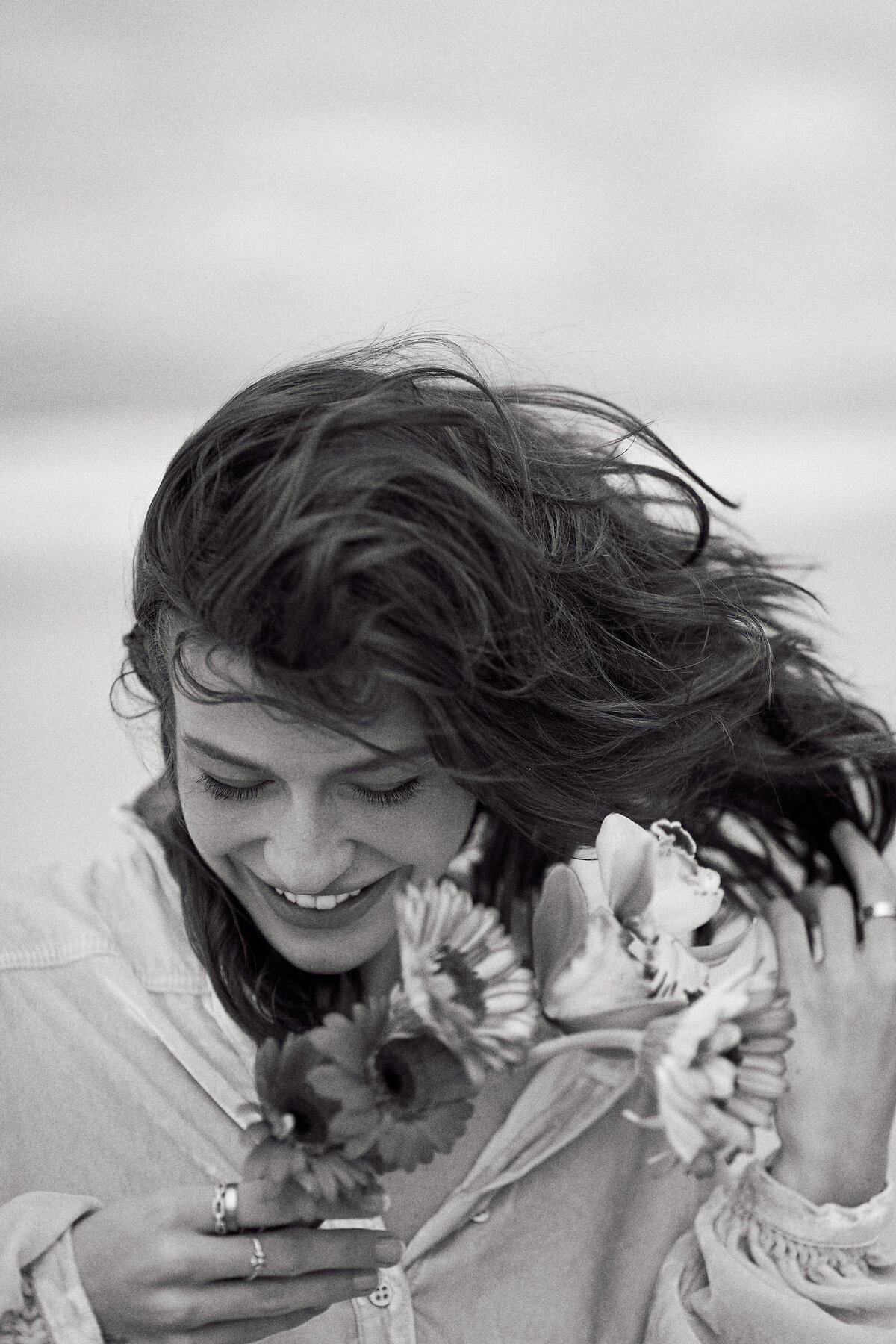 a representation of  a woman smiling down with the wind blowing in her brown hair while she holds a bundle of flowers
