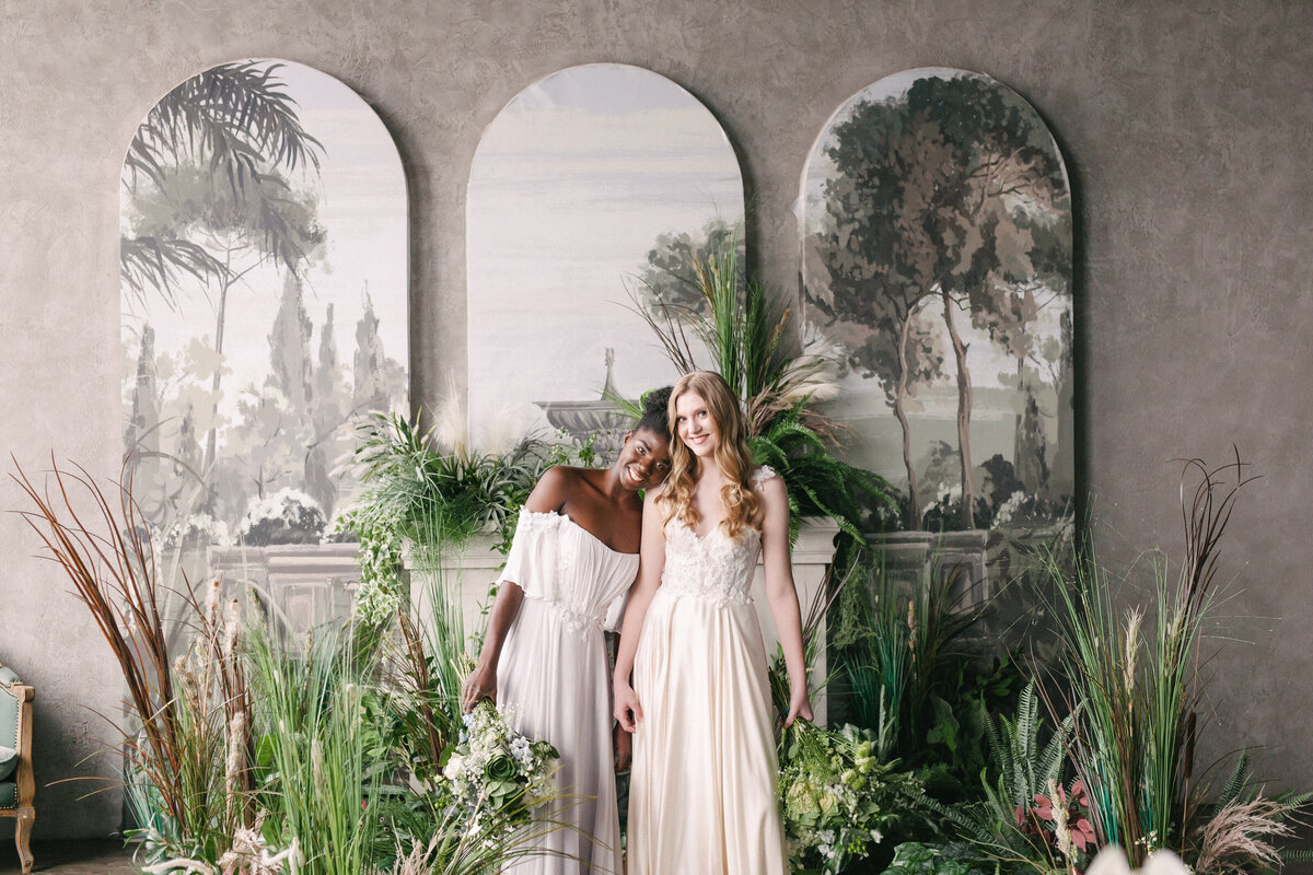 a couple of women standing next to each other surrounded by lush foliage