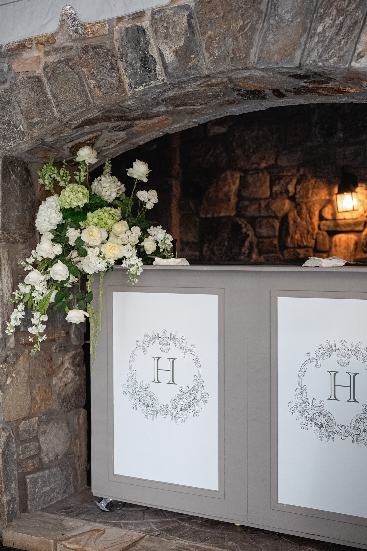 Custom monogrammed wedding bar decorated with lush white florals tucked into a stone alcove at a castle venue.
