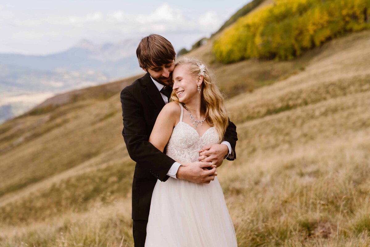 Groom hugging bride from behind as they smile in the golden hills of Telluride, Colorado