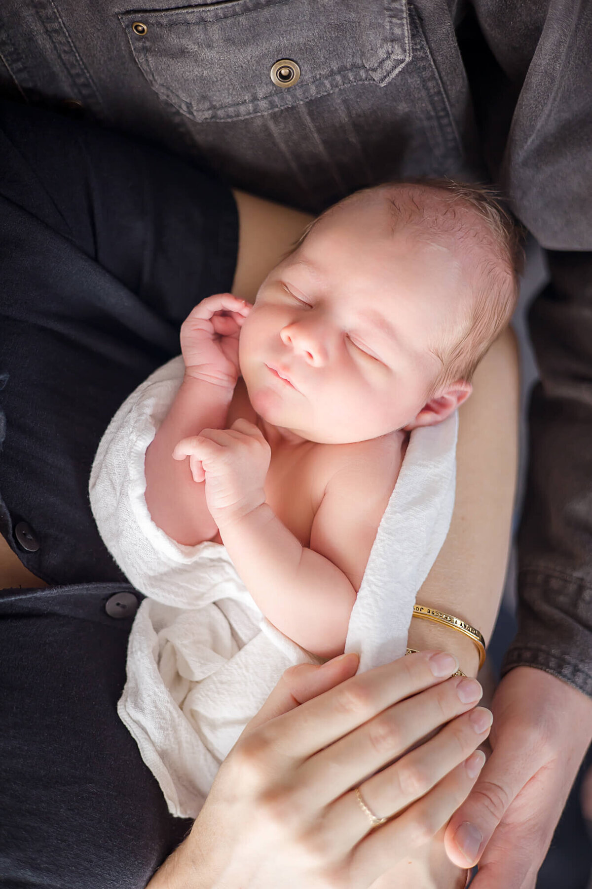 Newborn baby boy asleep in mom and dads arms, snuggling cozily