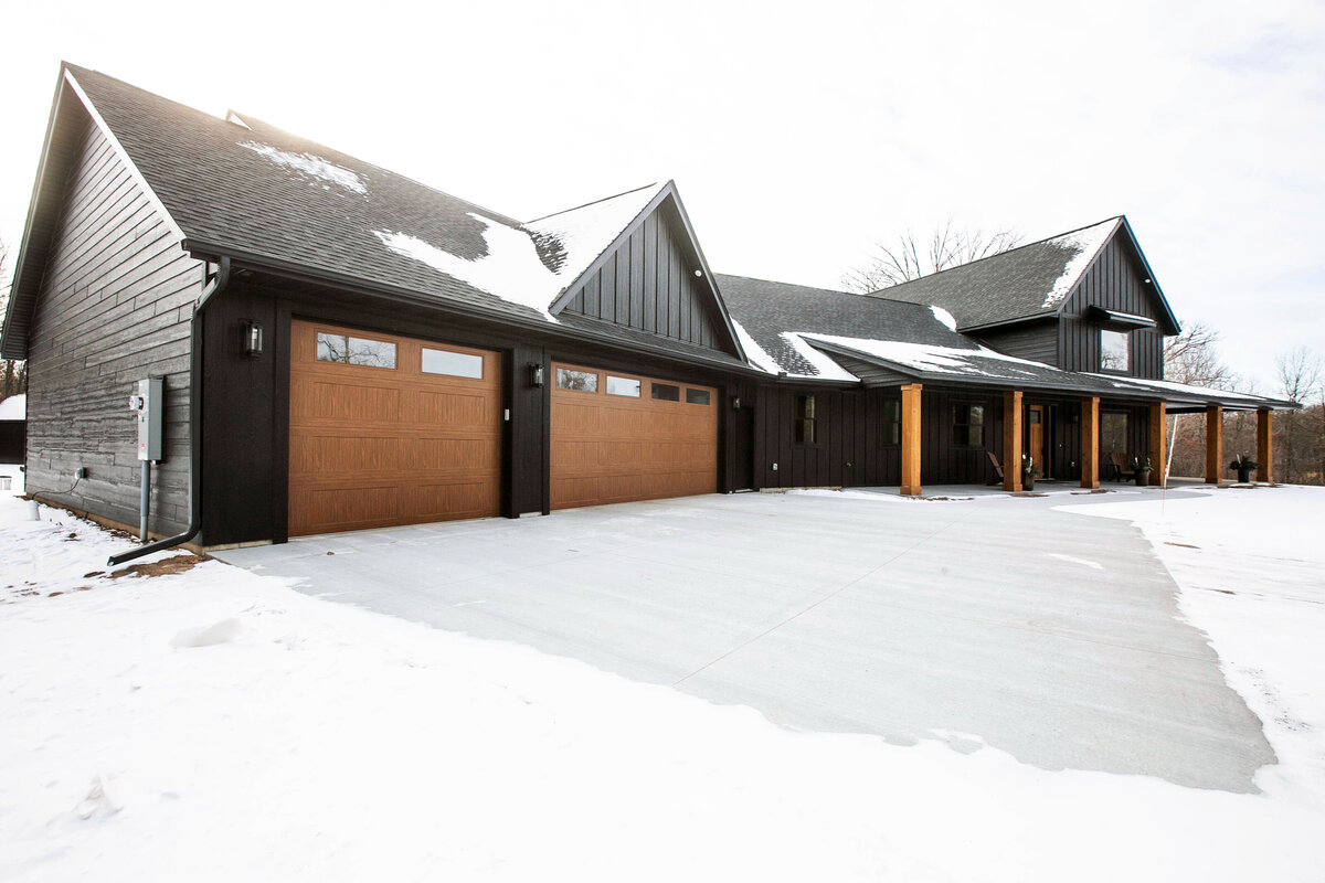 Exterior view of custom home in Elk River, Minnesota with black siding, wood details and front porch built by Cornerstone Custom Builds