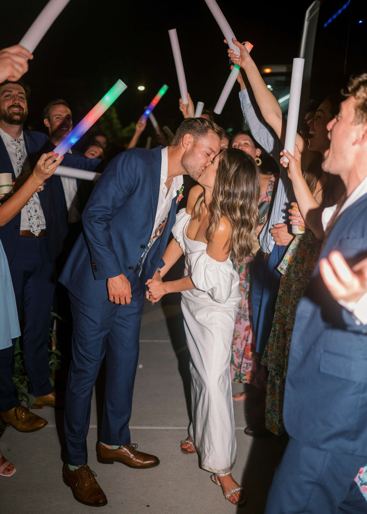 Virginia wedding photographer photographs bride and groom kissing while their friends wave colored light sticks during their grand exit.
