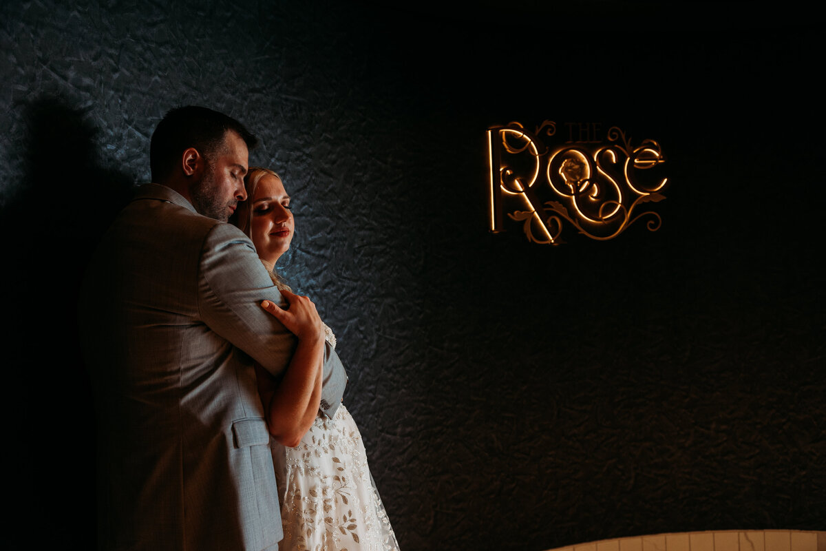Romantic wedding portrait inside The Rose lounge on the Disney Wish, with moody lighting and the gold Rose sign softly glowing beside the couple.