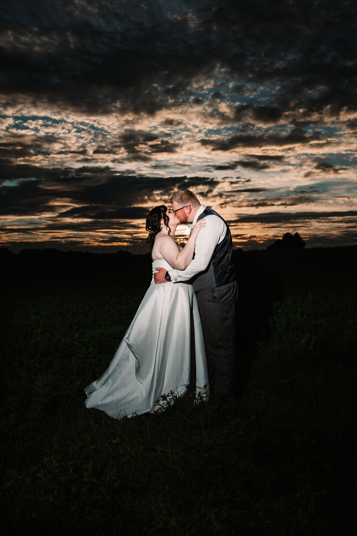 Newlyweds kiss in a field under an epic sunset