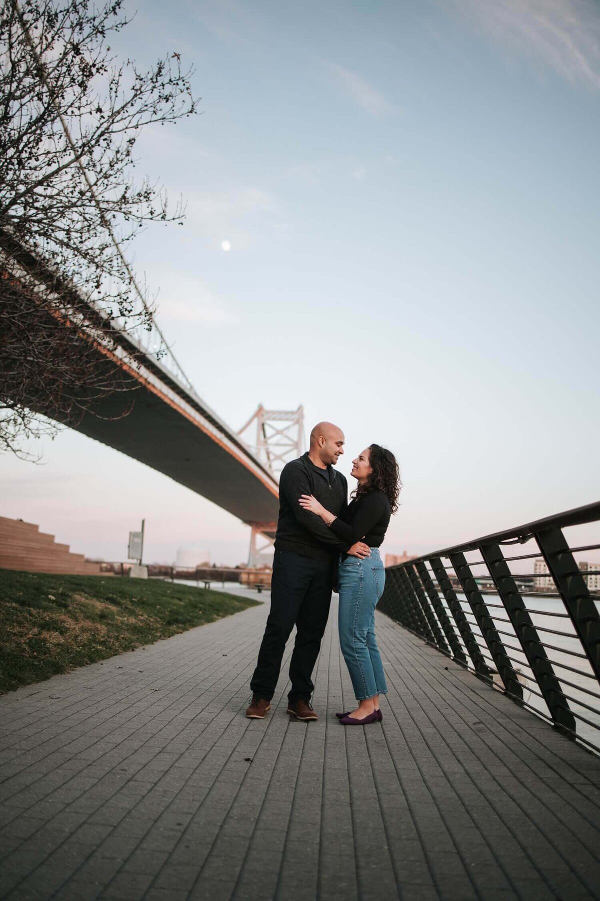 Couple in Philadelphia  standing next to bridge hugging each other.