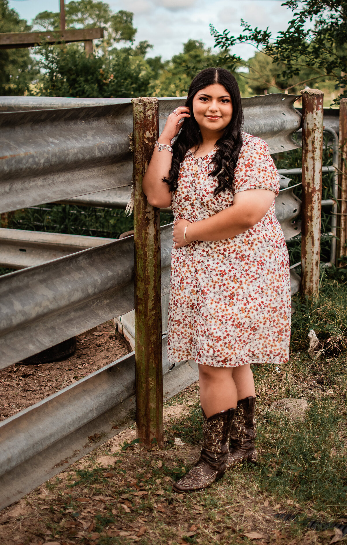 A graduate of aHouston high school tucks her hair behind her ear while she leans against a rustic tin fence.