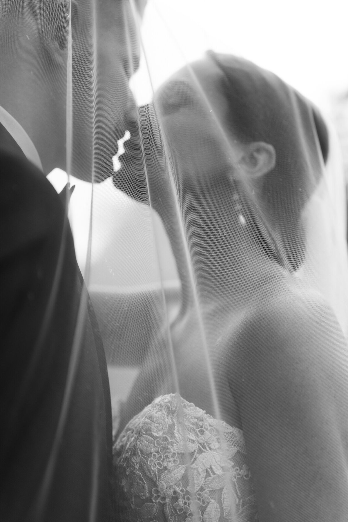Romantic black and white photo of bride and groom kissing under veil