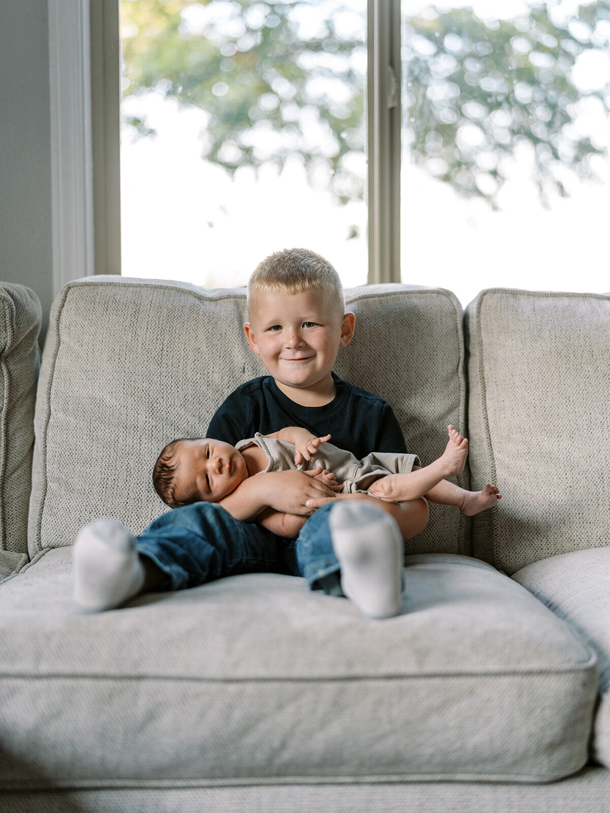 A young boy smiles at the camera while holding a baby.