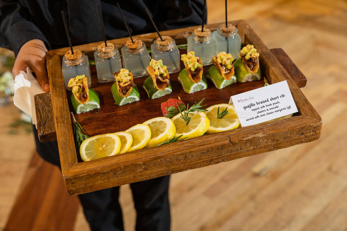 A person is holding a wooden tray filled with food and lemon slices.